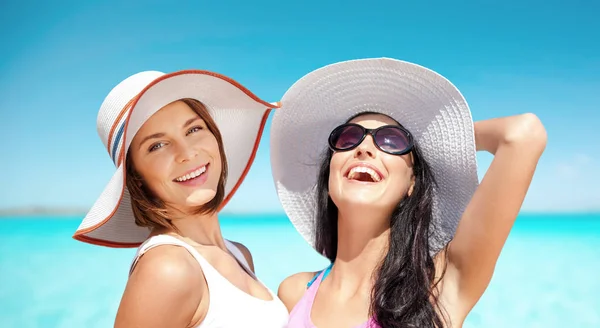 Glückliche junge Frauen mit Hüten am Sommerstrand — Stockfoto