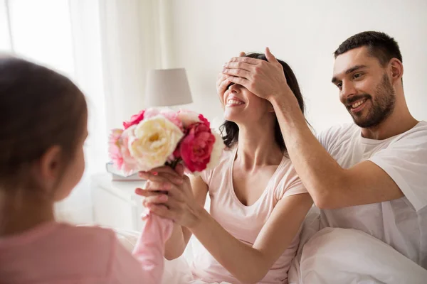 Feliz chica dando flores a la madre en la cama en casa — Foto de Stock