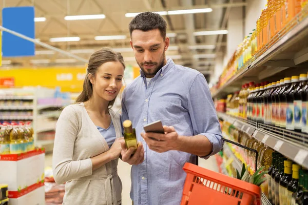 Paar mit Smartphone kauft Olivenöl im Supermarkt — Stockfoto