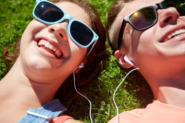 Heureux couple adolescent avec écouteurs couché sur l'herbe Images De Stock Libres De Droits