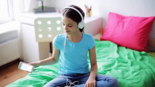 Chica feliz con teléfono inteligente y auriculares en casa — Vídeo de stock