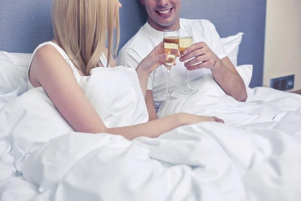 Casal sorridente com taças de champanhe na cama — Fotografia de Stock