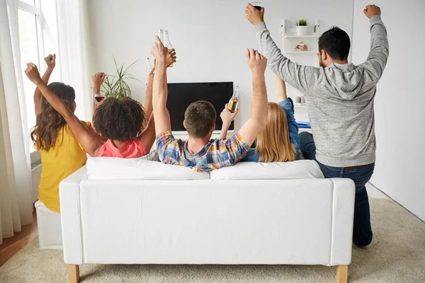 Vista traseira dos homens assistindo a um jogo de futebol na tv e sentado  em um sofá