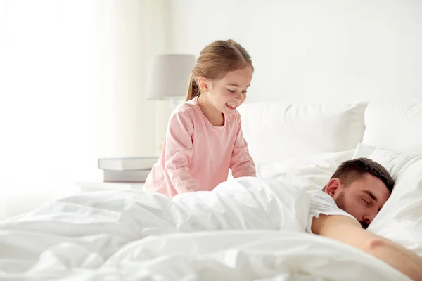 Klein meisje haar slapende vader wakker in bed — Stockfoto