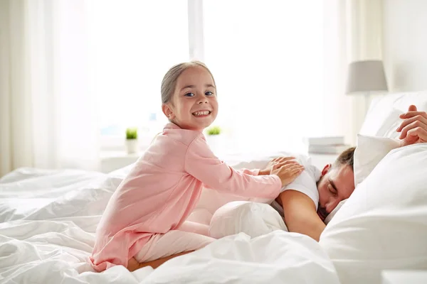 Little girl waking her sleeping father up in bed — Stock Photo, Image