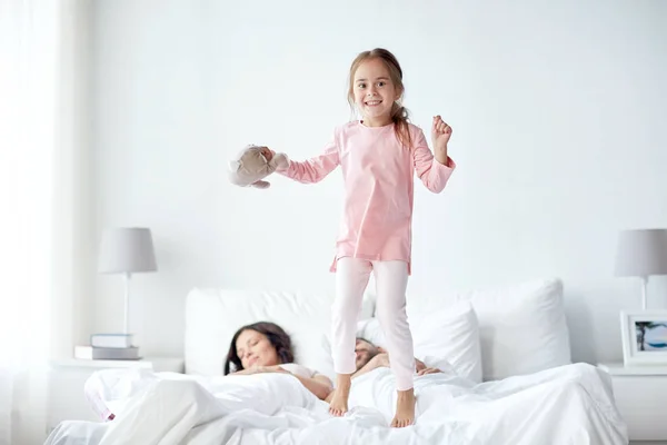 Bambino felice con giocattolo e genitori a letto a casa — Foto Stock