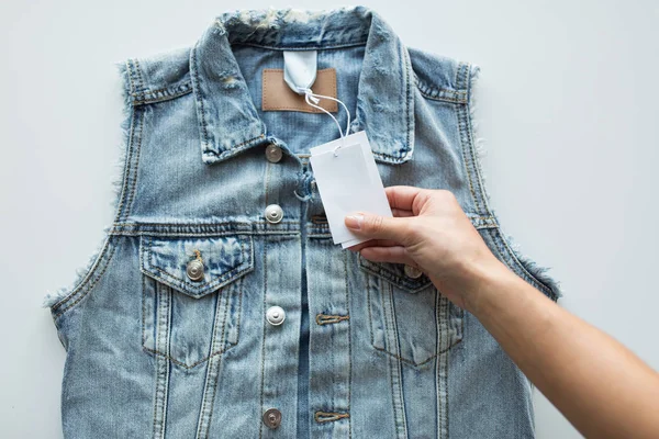 Close up of hand holding price tag of denim vest — Stock Photo, Image