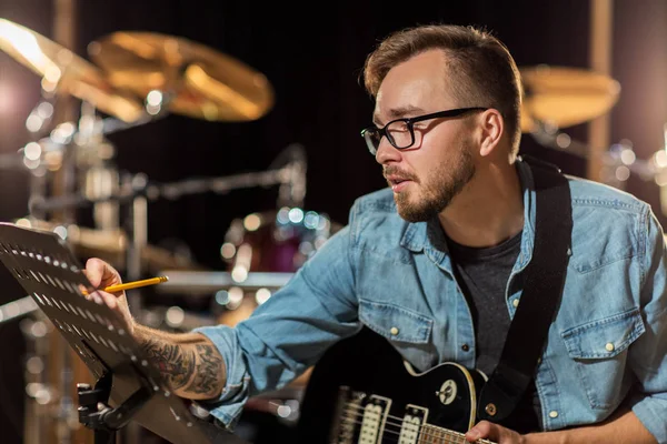 Mannen med gitarr skriver till notbok på studio — Stockfoto