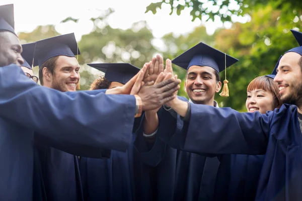 Happy students in mortar boards making high five — Stock Photo, Image