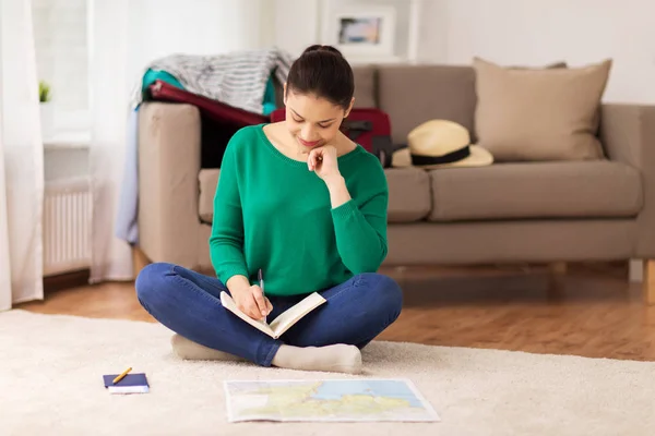 Mujer con cuaderno y mapa de viajes en casa — Foto de Stock