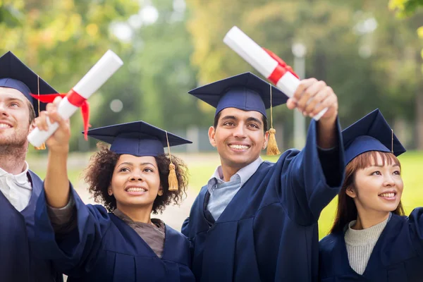 Happy students in mortar boards with diplomas Stock Image