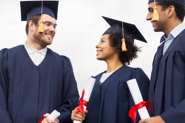 Happy students in mortar boards with diplomas — Stock Photo, Image