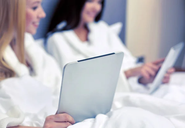 Happy women in bathrobes with tablet pc at hotel — Stock Photo, Image