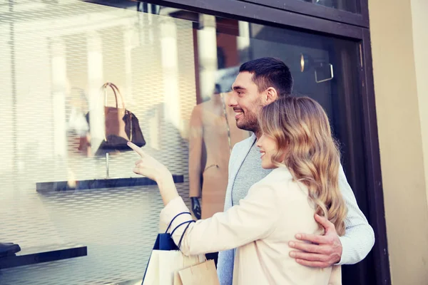 Casal feliz com sacos de compras na vitrine da loja — Fotografia de Stock