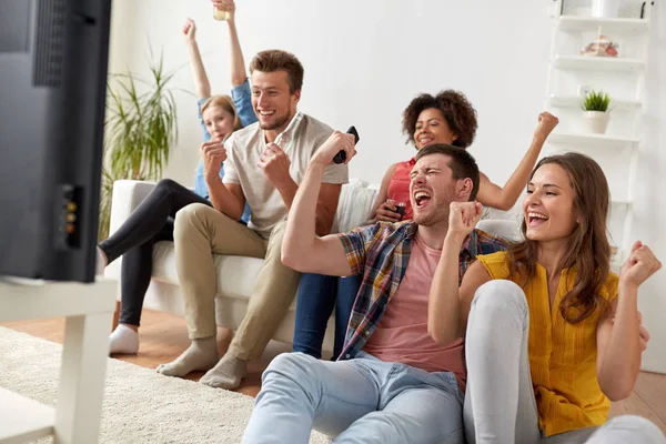 Amigos felizes com controle remoto assistindo tv em casa — Fotografia de Stock