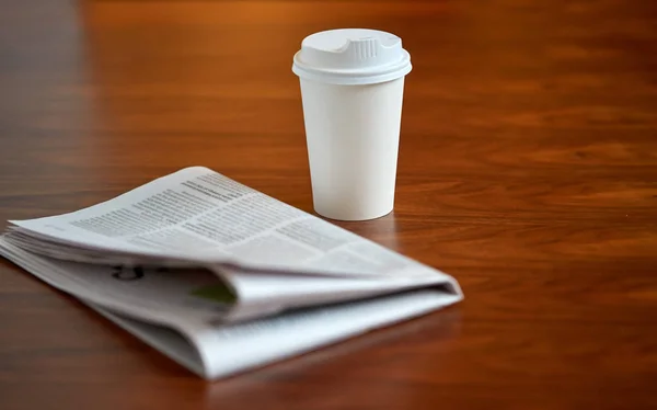 Kaffeetrinken in Pappbecher und Zeitung auf dem Tisch — Stockfoto