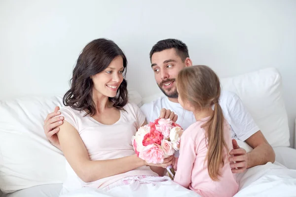 Menina feliz dando flores para a mãe na cama em casa — Fotografia de Stock