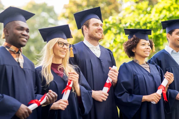 Glada studenter i murbruk styrelser med diplom — Stockfoto