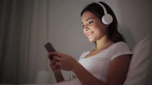 Mujer con smartphone y auriculares en la cama — Vídeos de Stock