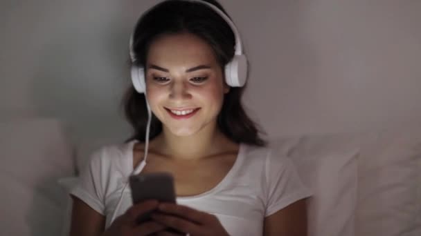 Woman with smartphone and headphones in bed — Stock Video