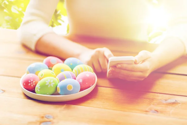 Close up of hands with easter eggs and smartphone — Stock Photo, Image