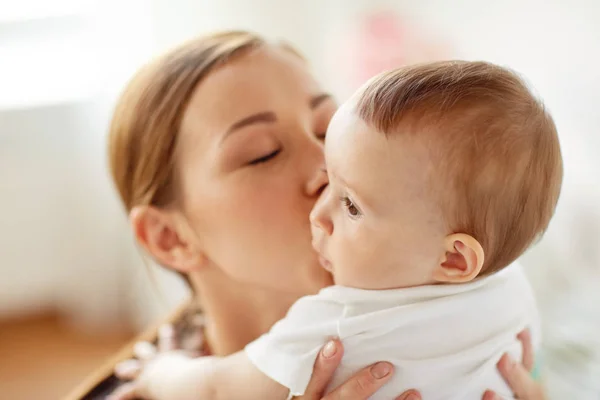 Feliz jovem mãe beijando bebê em casa — Fotografia de Stock