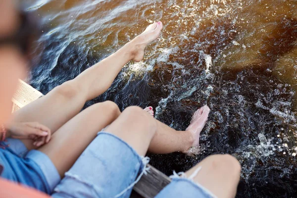 Gambe di giovane coppia seduta sul fiume ormeggio — Foto Stock