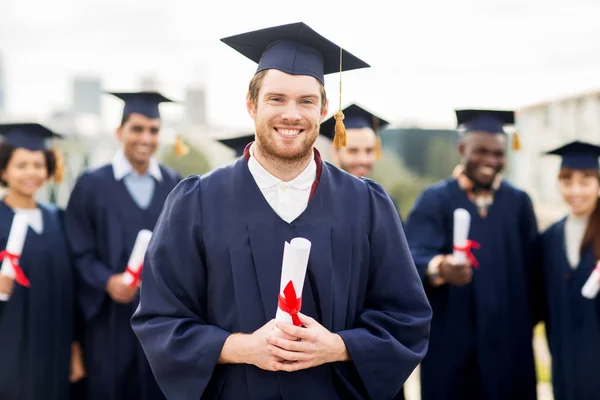 Glada studenter i murbruk styrelser med diplom — Stockfoto