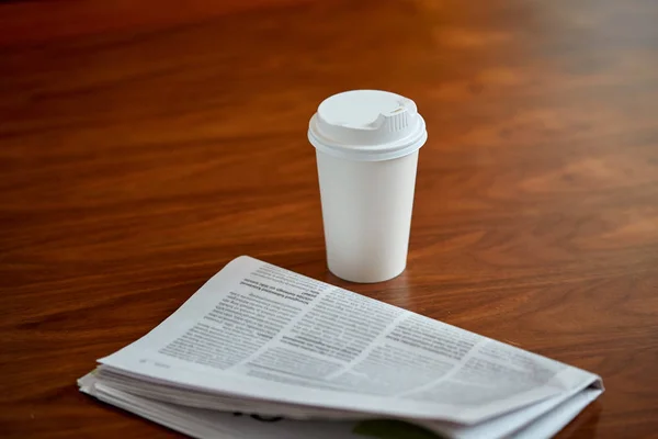 Kaffeetrinken in Pappbecher und Zeitung auf dem Tisch — Stockfoto