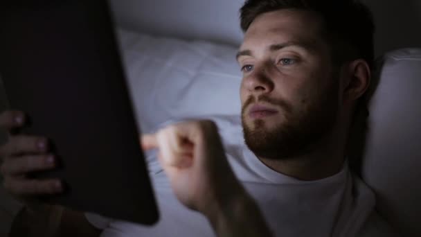 Hombre joven con tableta pc en la cama en el dormitorio en casa — Vídeo de stock