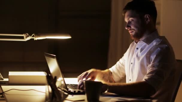 Человек с ноутбуком и смартфоном работает в ночном офисе — стоковое видео