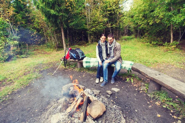 Casal feliz sentado no banco perto de fogo acampamento — Fotografia de Stock