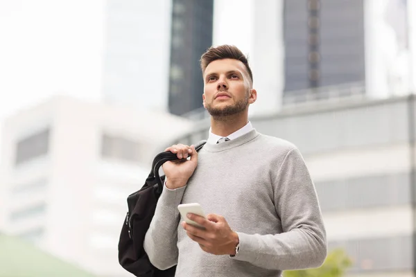 young man with smartphone and bag in city