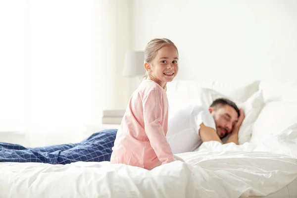 Little girl waking her sleeping father up in bed — Stock Photo, Image