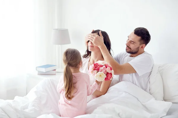 Feliz chica dando flores a la madre en la cama en casa — Foto de Stock