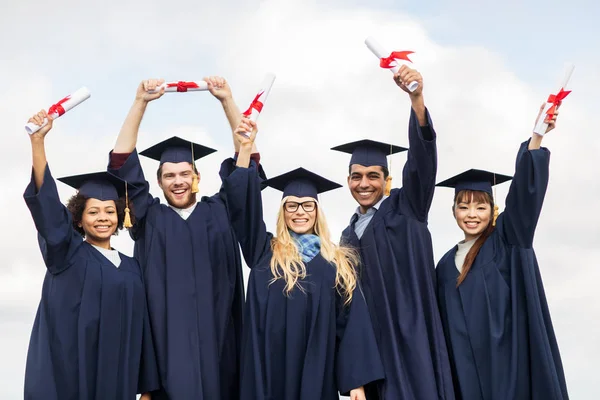 Estudantes felizes em placas de argamassa acenando diplomas — Fotografia de Stock