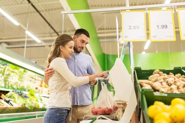 Casal feliz pesando tomates em escala no supermercado — Fotografia de Stock