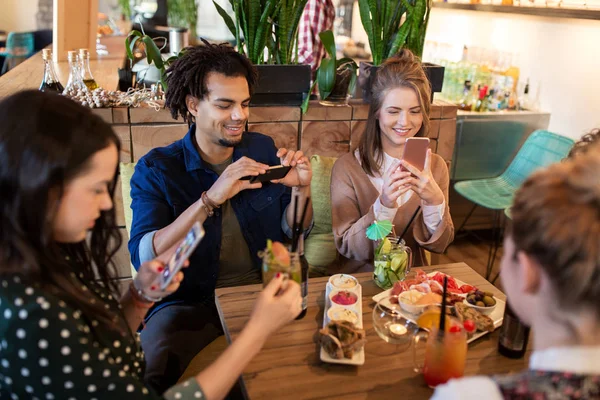 Amigos com smartphones e comida no restaurante — Fotografia de Stock