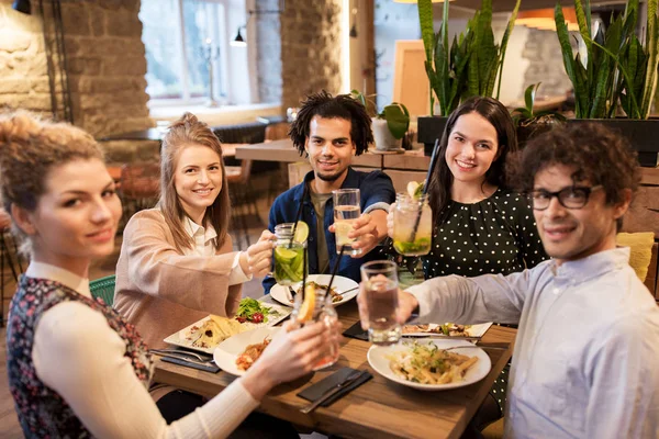 Happy friends with drinks and food at restaurant — Stock Photo, Image