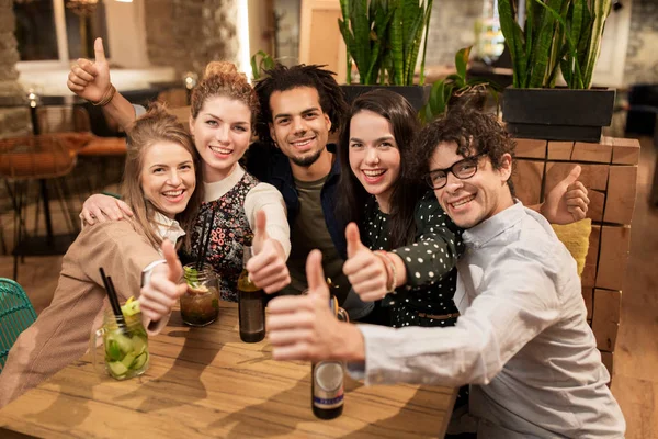 Happy friends with drinks showing thumbs up at bar — Stock Photo, Image