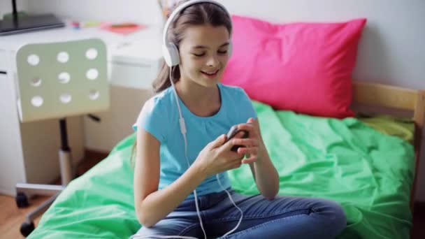 Chica feliz con teléfono inteligente y auriculares en casa — Vídeo de stock