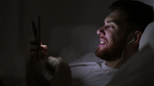 Uomo con smartphone e auricolari a letto di notte — Video Stock