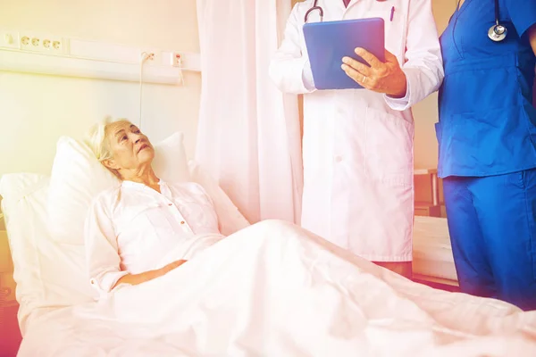 Médico e enfermeira visitando mulher idosa no hospital — Fotografia de Stock