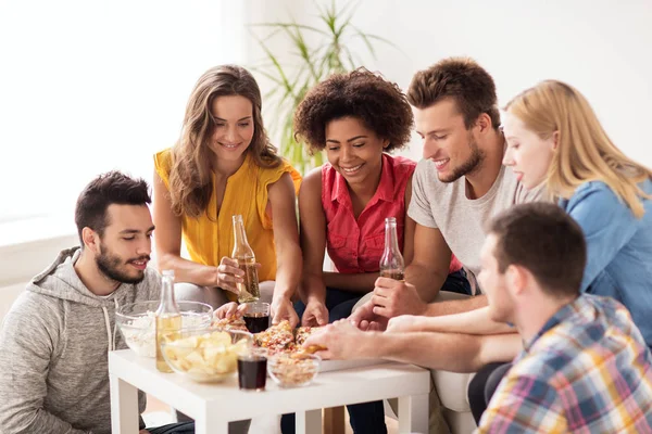 Amigos felizes com bebidas comer pizza em casa — Fotografia de Stock