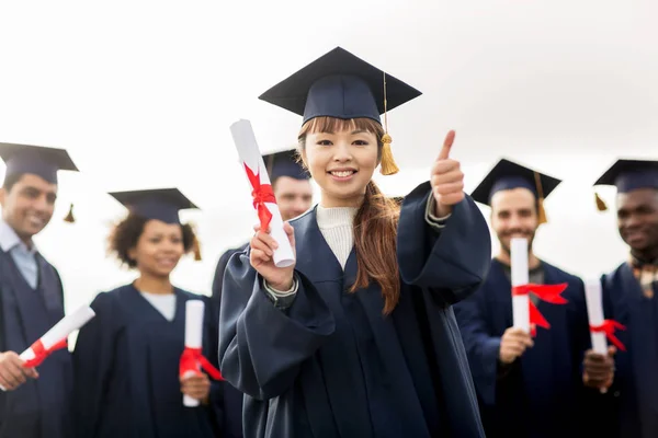 Happy students with diplomas showing thumbs up — Stock Photo, Image