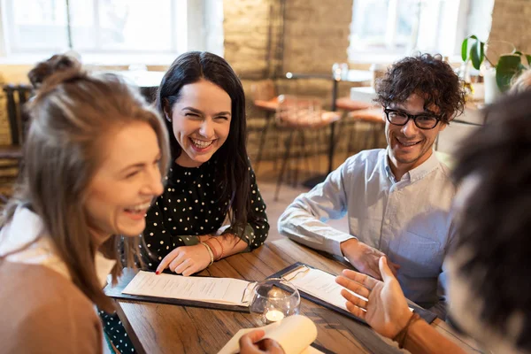 Happy friends with menu at restaurant — Stock Photo, Image