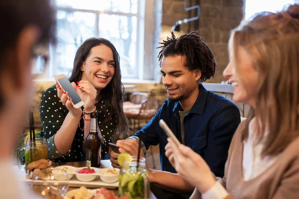Amigos com smartphones e comida no bar ou café — Fotografia de Stock