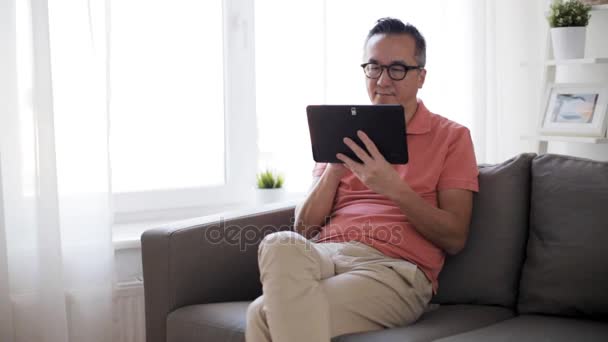 Hombre con tablet pc sentado en el sofá en casa — Vídeo de stock