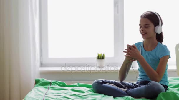 Chica feliz con teléfono inteligente y auriculares en casa — Vídeo de stock