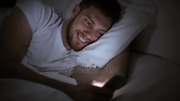 Mladý muž s chytrým telefonem v posteli v noci — Stock video